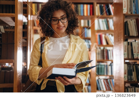 Book in blue hard cover is in hands. Beautiful woman is in the library Book in blue hard cover is in hands. Beautiful woman is in the library 136823649