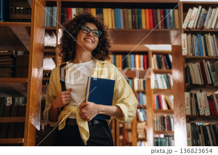 Holding the book. Beautiful woman is in the library 136823654