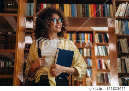 Holding the book. Beautiful woman is in the library 136823655