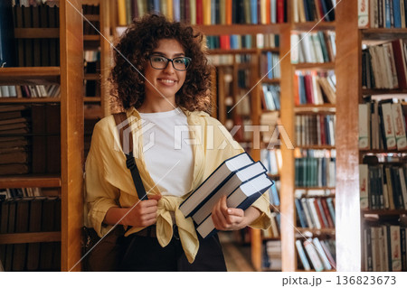 Bunch of books are in hands. Beautiful woman is in the library 136823673