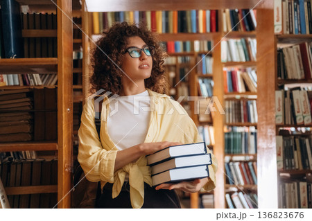 Bunch of books are in hands. Beautiful woman is in the library Bunch of books are in hands. Beautiful woman is in the library 136823676