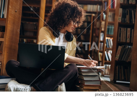 Working by using laptop. Beautiful woman is in the library Working by using laptop. Beautiful woman is in the library 136823695