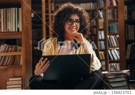 Laptop is on legs. Beautiful woman is in the library Laptop is on legs. Beautiful woman is in the library 136823701