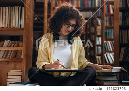 The writing process. With pen and headphones. Beautiful woman is in the library 136823708