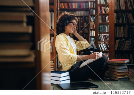 Listening to music and writing. Beautiful woman is in the library 136823717