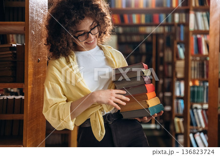 Colorful covers on books. Holding them. Beautiful woman is in the library 136823724