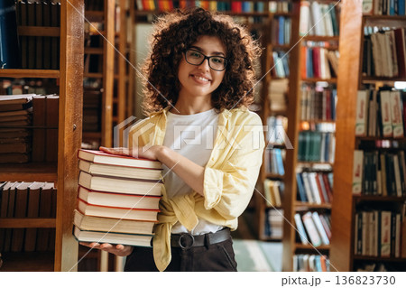That's a lot of books in hands. Beautiful woman is in the library That's a lot of books in hands. Beautiful woman is in the library 136823730