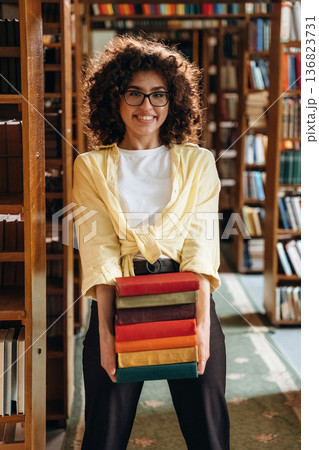 Standing and smiling. Beautiful woman is in the library Standing and smiling. Beautiful woman is in the library 136823731