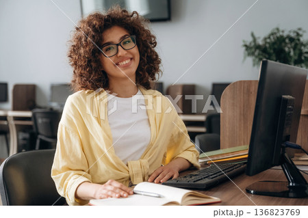 By the table with pen and notepad. Woman is in the library section with computers By the table with pen and notepad. Woman is in the library section with computers 136823769