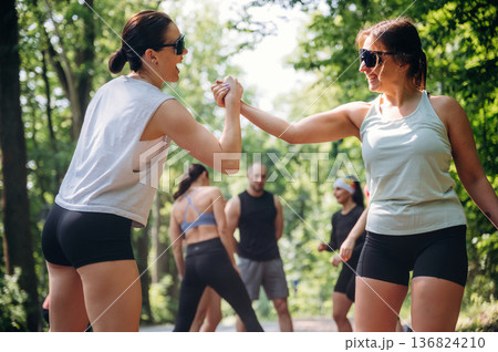 Two women are doing handshake type, together, teamwork conception. Group of runners are together outdoors Two women are doing handshake type, together, teamwork conception. Group of runners are together outdoors 136824210