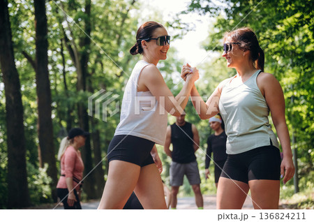 Two women are doing handshake type, together, teamwork conception. Group of runners are together outdoors Two women are doing handshake type, together, teamwork conception. Group of runners are together outdoors 136824211