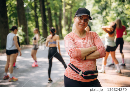 With arms crossed, woman is standing. Group of runners are together outdoors With arms crossed, woman is standing. Group of runners are together outdoors 136824270