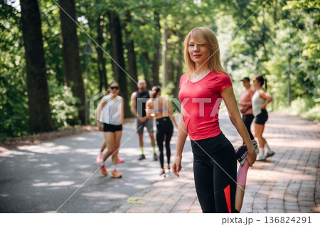 Blonde woman is standing in front of people. Group of runners are together outdoors 136824291