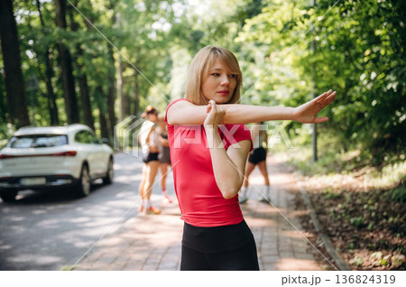 Blonde woman is standing in front of people. Group of runners are together outdoors Blonde woman is standing in front of people. Group of runners are together outdoors 136824319