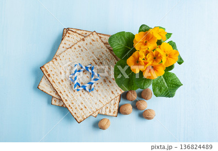 Passover holiday card with matzah, walnuts, yellow spring flowers on light blue background, gold and white accents, copy space 136824489