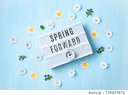 Daylight saving Time, Spring forward, Summer back concept. White Alarm Clock and Spring Daisy Flowers on Blue Background Daylight saving Time, Spring forward, Summer back concept. White Alarm Clock and Spring Daisy Flowers on Blue Background 136824878