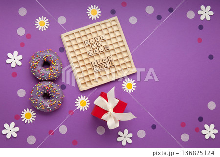 Give to Gain concept for International Women's Day, 8 march. Two purple doughnuts, red gift box and spring flowers, top view flat lay Give to Gain concept for International Women's Day, 8 march. Two purple doughnuts, red gift box and spring flowers, top view flat lay 136825124