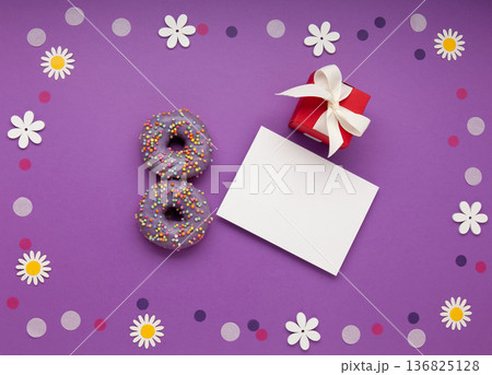 Give to Gain concept for International Women's Day, 8 march. Two purple doughnuts, red gift box and spring flowers, top view flat lay Give to Gain concept for International Women's Day, 8 march. Two purple doughnuts, red gift box and spring flowers, top view flat lay 136825128
