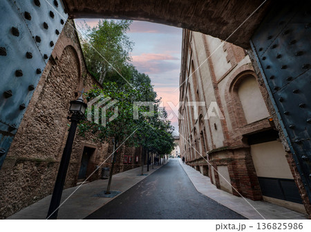 Scenic view through an ancient stone archway of a narrow street at Montserrat Monastery, Spain, during a beautiful sunset with pink clouds in the sky Scenic view through an ancient stone archway of a narrow street at Montserrat Monastery, Spain, during a beautiful sunset with pink clouds in the sky 136825986
