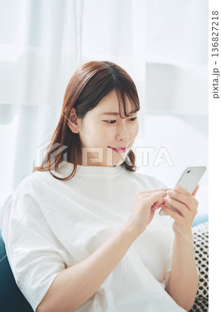 自宅のリビングでスマートフォンを操作する30代女性のライフスタイル 自宅のリビングでスマートフォンを操作する30代女性のライフスタイル 136827218