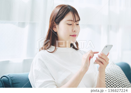 自宅のリビングでスマートフォンを操作する30代女性のライフスタイル 自宅のリビングでスマートフォンを操作する30代女性のライフスタイル 136827224