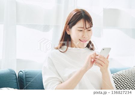 自宅のリビングでスマートフォンを操作する30代女性のライフスタイル 自宅のリビングでスマートフォンを操作する30代女性のライフスタイル 136827234