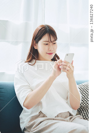 自宅のリビングでスマートフォンを操作する30代女性のライフスタイル 136827240
