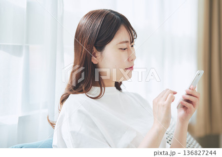 自宅のリビングでスマートフォンを操作する30代女性のライフスタイル 自宅のリビングでスマートフォンを操作する30代女性のライフスタイル 136827244