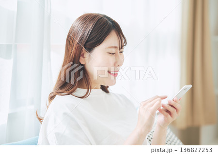 自宅のリビングでスマートフォンを操作する30代女性のライフスタイル 136827253