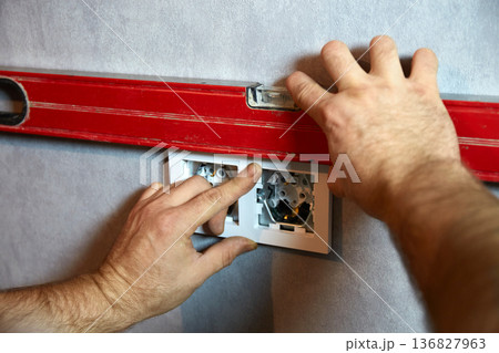 A worker uses a building level to ensure the electric outlet is straight. A worker uses a building level to ensure the electric outlet is straight. 136827963