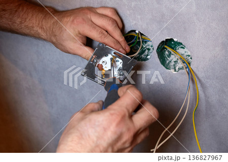A worker installs an electrical outlet into a wall using a screwdriver A worker installs an electrical outlet into a wall using a screwdriver 136827967