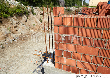 A construction site features a newly built brick wall with visible rebar bars extending from the concrete foundation A construction site features a newly built brick wall with visible rebar bars extending from the concrete foundation 136827989