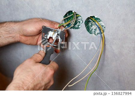 A worker installs an electrical outlet into a wall using a screwdriver A worker installs an electrical outlet into a wall using a screwdriver 136827994