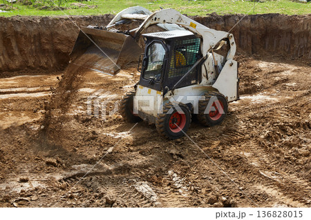 Heavy machinery moves dirt at a construction site with a clear focus on ground leveling and preparation for building Heavy machinery moves dirt at a construction site with a clear focus on ground leveling and preparation for building 136828015