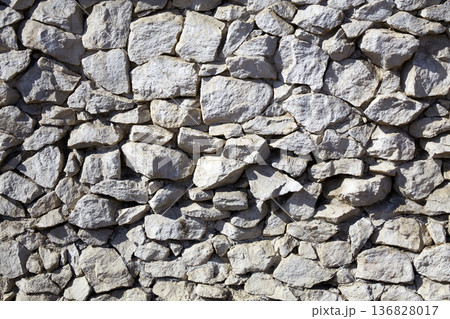 Natural stone wall showcases varied textures and colors in an outdoor setting during daylight hours 136828017