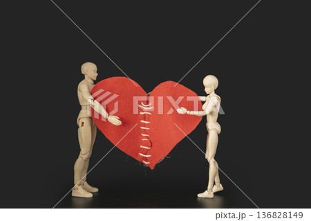 Conceptual image of two plastic mannequins holding a large red heart with stitches, symbolizing reconciliation, healing a broken heart, and saving a relationship 136828149