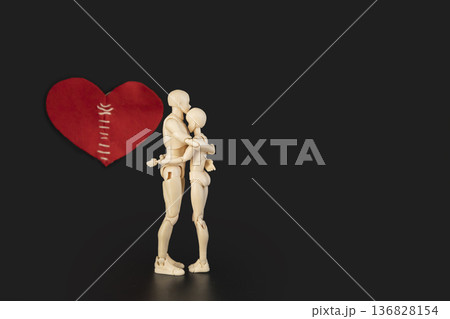 Conceptual image of two plastic mannequins hugging each other and on background a large red heart with stitches, symbolizing reconciliation, healing a broken heart, and saving a relationship 136828154