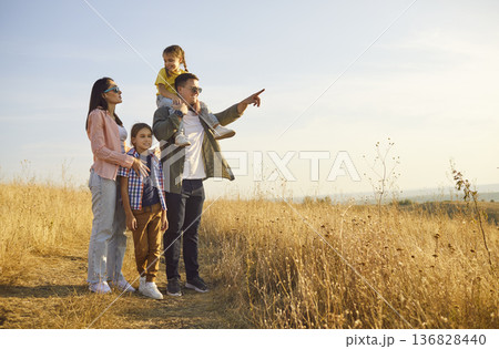 Cheerful family enjoying golden hour walk, kids riding shoulders at sunset Cheerful family enjoying golden hour walk, kids riding shoulders at sunset 136828440