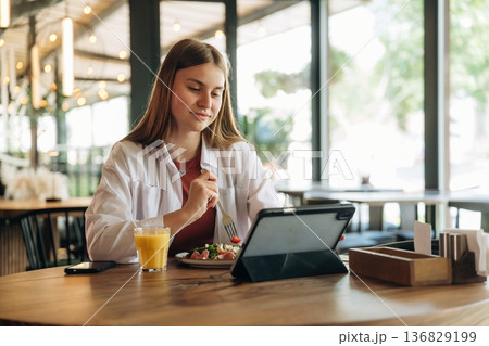 Eating, digital tablet is on the table. Young woman is in the cafe at daytime Eating, digital tablet is on the table. Young woman is in the cafe at daytime 136829199
