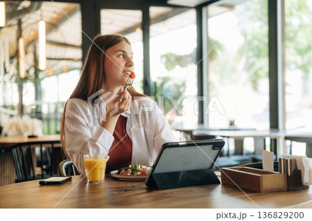 Eating, digital tablet is on the table. Young woman is in the cafe at daytime 136829200