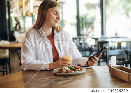 Having good time, with food and smartphone. Young woman is in the cafe at daytime Having good time, with food and smartphone. Young woman is in the cafe at daytime 136829229