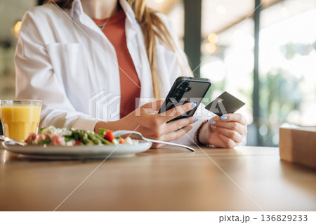 Credit or debit card and smartphone. Close up view of teenage girl that is sitting in the cafe restaurant Credit or debit card and smartphone. Close up view of teenage girl that is sitting in the cafe restaurant 136829233