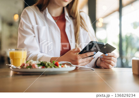 Credit or debit card and smartphone. Close up view of teenage girl that is sitting in the cafe restaurant Credit or debit card and smartphone. Close up view of teenage girl that is sitting in the cafe restaurant 136829234
