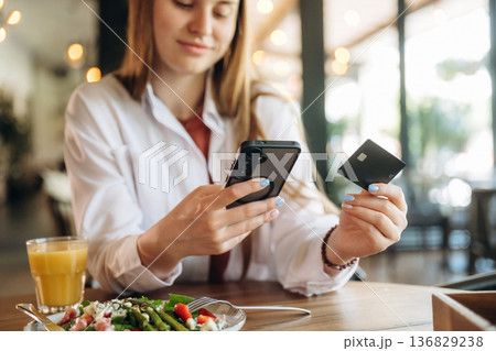 Front view, smartphone and credit card, payment. Young woman is in the cafe at daytime 136829238