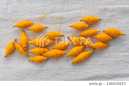 Yellow thread roll with bamboo tube placed on a white cotton background. 136829833