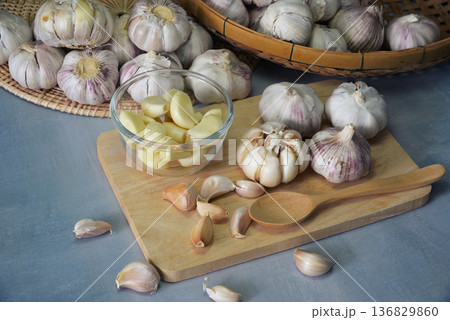 Close-up shot of garlic laying on wooden chopping board on concrete table In the kitchen, peel them in a glass bowl prepared for use as a food ingredient. 136829860
