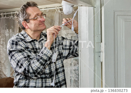 After securing surveillance camera bracket above door, farmer connects power. 136830273