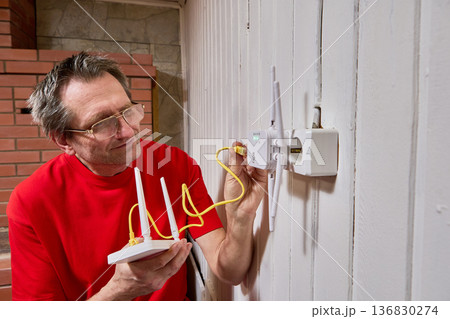 Connection of wifi router with repeater using LAN cable mature man adjusts equipment for internet distribution in rural house. 136830274