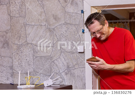 Issue with setting up wifi distribution equipment elderly man uses smartphone to find solution on internet. 136830276