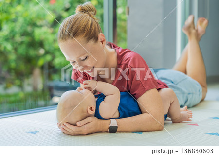 Mother and baby lying on a soft play mat at home, playing, talking and sharing a joyful moment together. Authentic family lifestyle, early childhood development and emotional bonding. Parenting and 136830603